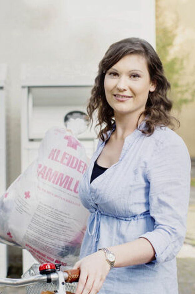Kleidersammlung des DRK und Altkleidercontainer: junge Frau mit Altkleidersack vor einem Container des DRK- 2014