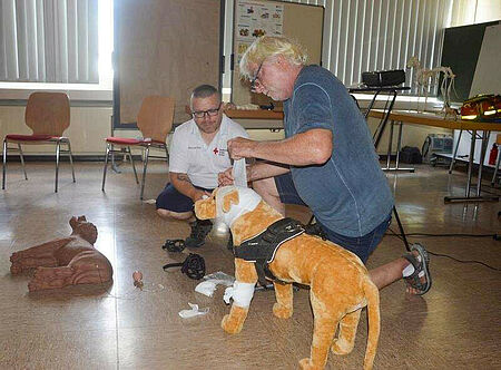 EH am Hund Ausbildungsleiter Manuel Hauck (links) zeigt an Stofftieren, was beim Verbinden zu beachten ist. Links befindet sich ein Hund in möglicherweise lebensrettender Position.