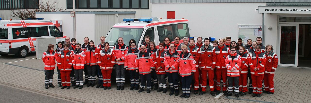 Mehrere DRK-Helfer stehen vor einem Gebäude. Im Hintergrund sind 2 Einsatzfahrzeuge zu sehen. Mehrere DRK-Helfer stehen vor einem Gebäude. Im Hintergrund sind 2 Einsatzfahrzeuge zu sehen.
